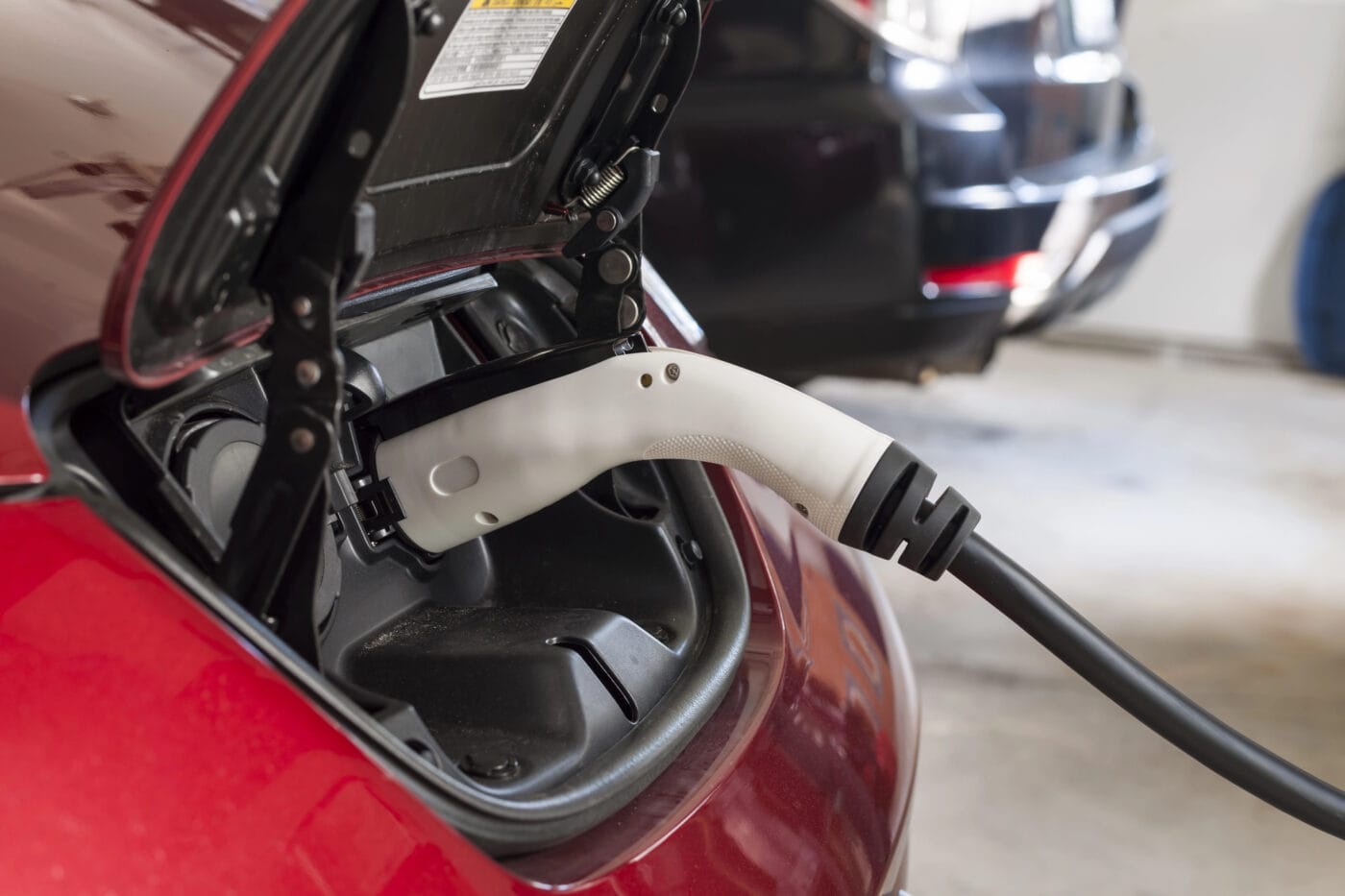 Electric vehicle charging with a black and white charging cable connected to a red car.